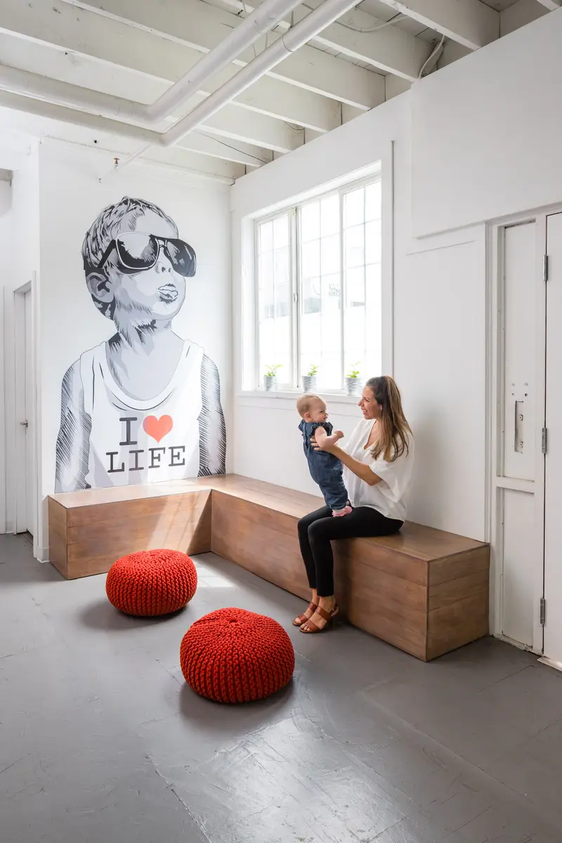 A parent and baby in the waiting area at Revolution Health in Vancouver, beside the I Heart Life mural